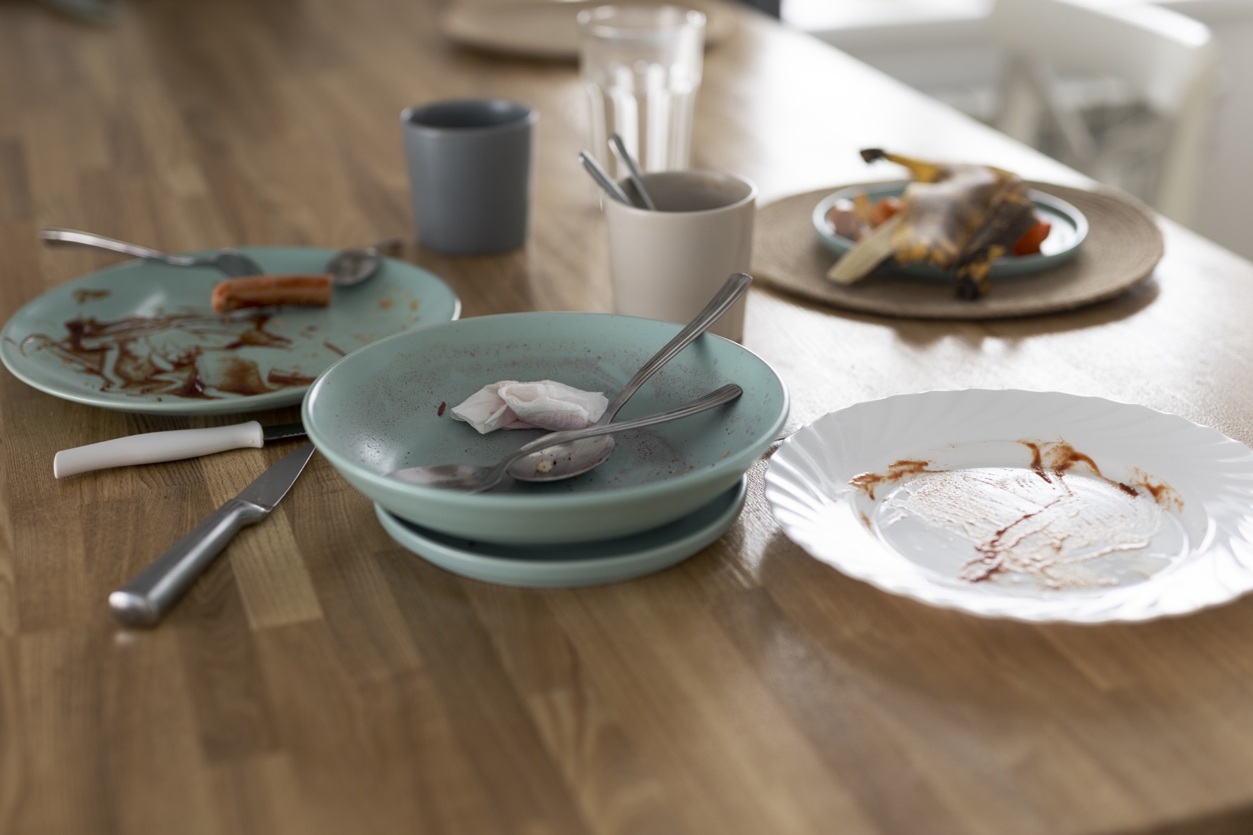 Dirty dishes, turquoise plates with leftover food and glasses spread across a wooden dining table
