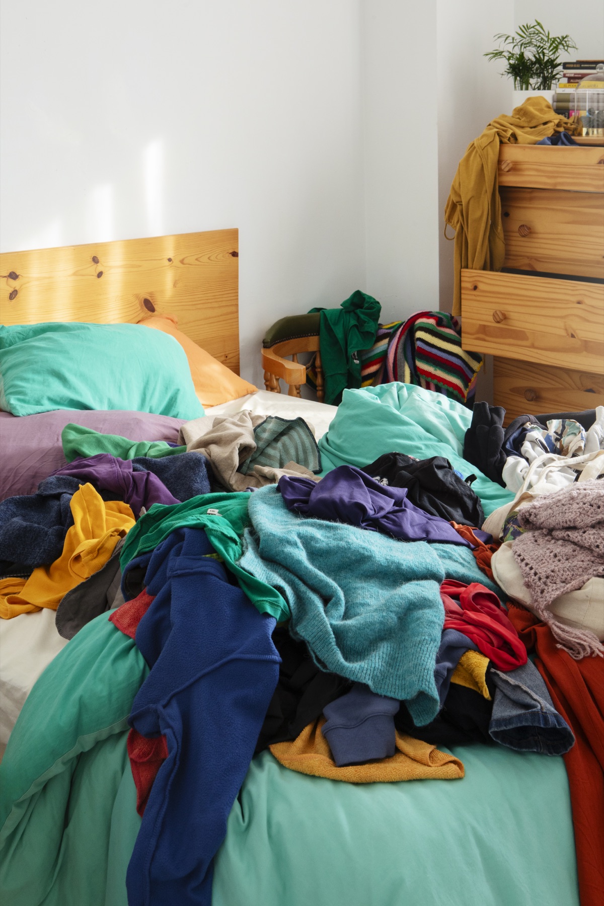 A bed and bedroom covered with piles of clothes and household items